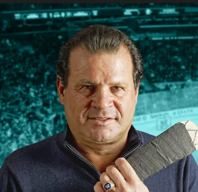 Man holding a hockey stick grip with a stadium crowd in the background.