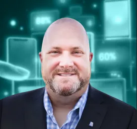 Smiling bald man with beard wearing a checkered shirt and dark blazer in front of digital graphics.