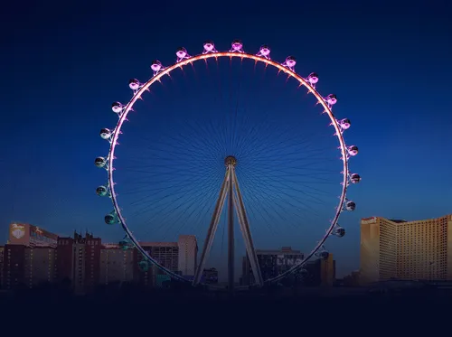 The Linq Ferris wheel lit with pink lights against a twilight sky with city buildings below.