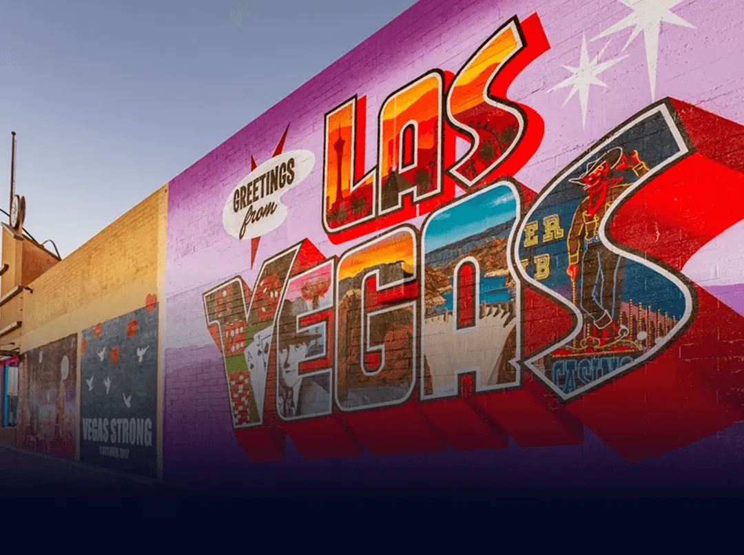 Colorful mural with text 'Greetings from Las Vegas' on a purple wall depicting iconic city images.
