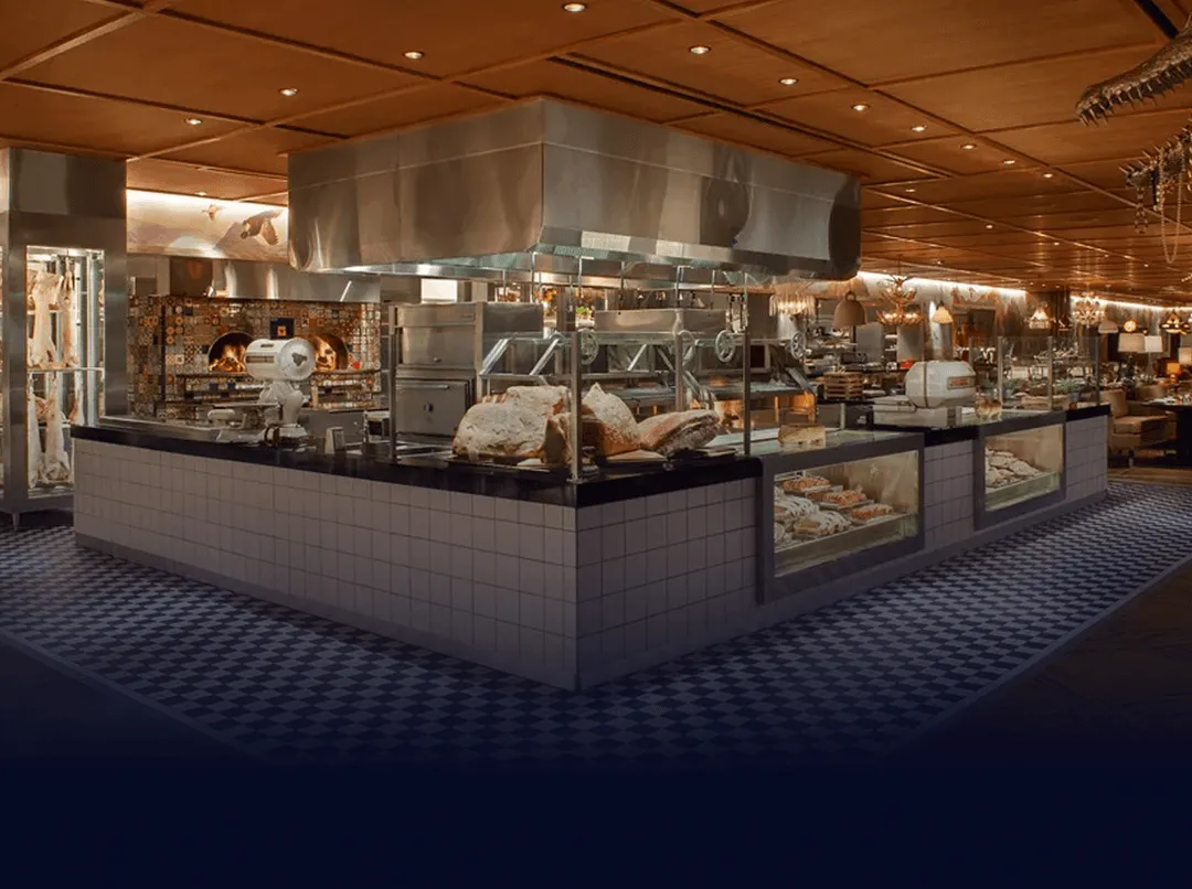 Modern restaurant kitchen with tiled counters, exposed meat, ovens, and warm lighting.