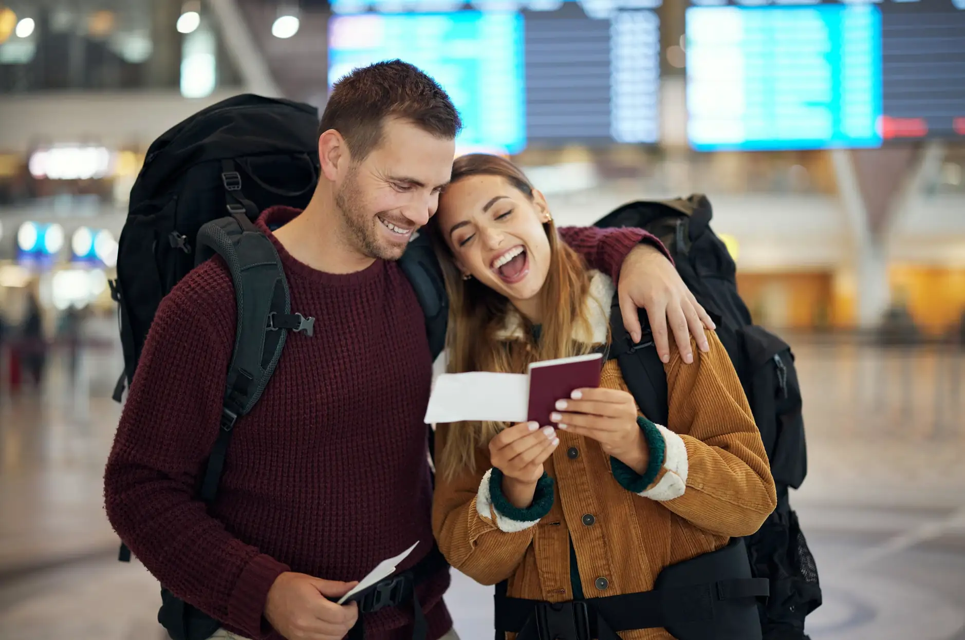 Happy couple with backpacks looking at their passport and boarding pass at an airport.