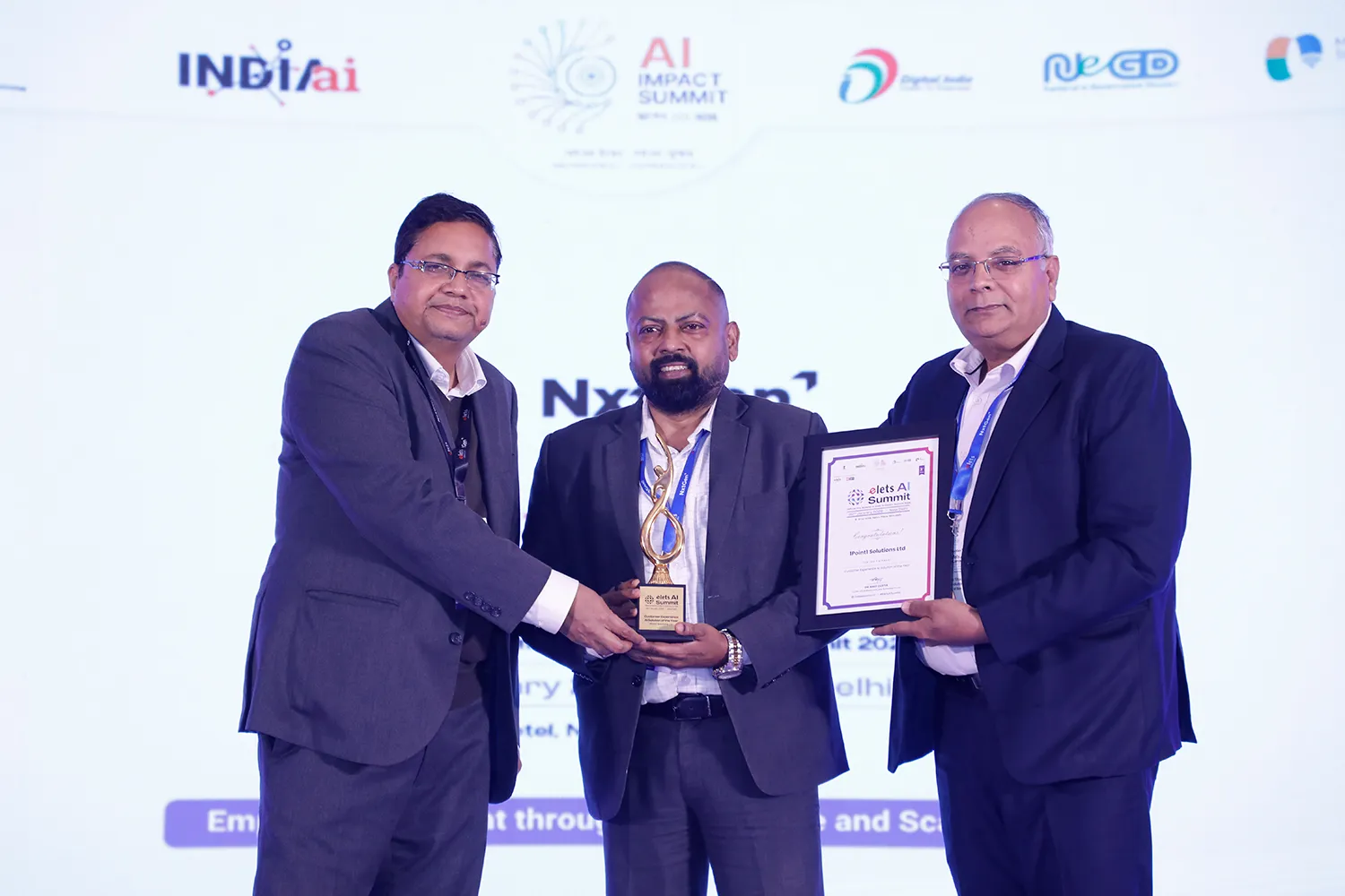 Three men in suits on stage holding an award and certificate at AI Impact Summit event.