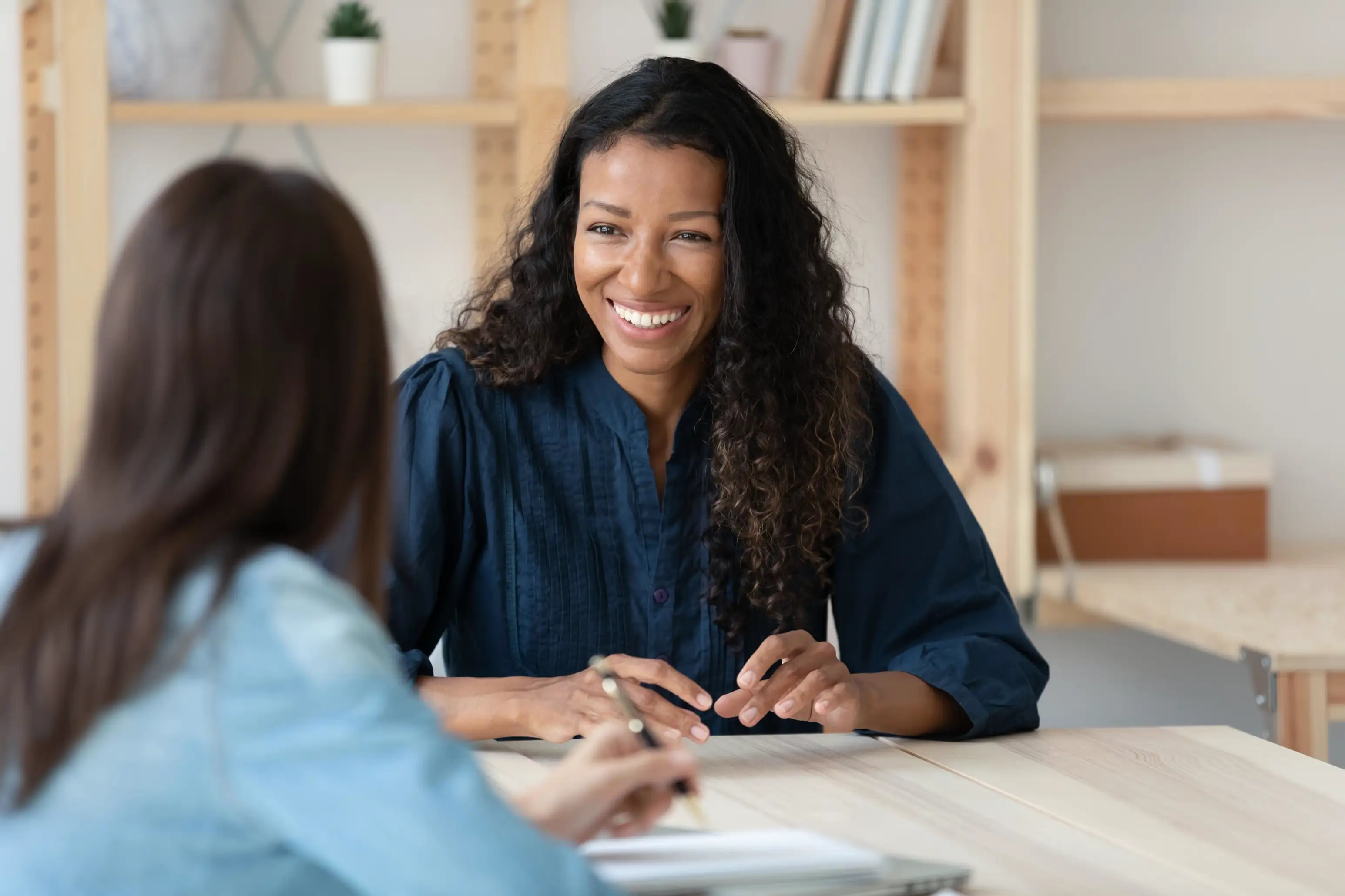 Two women having a friendly discussion across a table in a bright, casual office space.