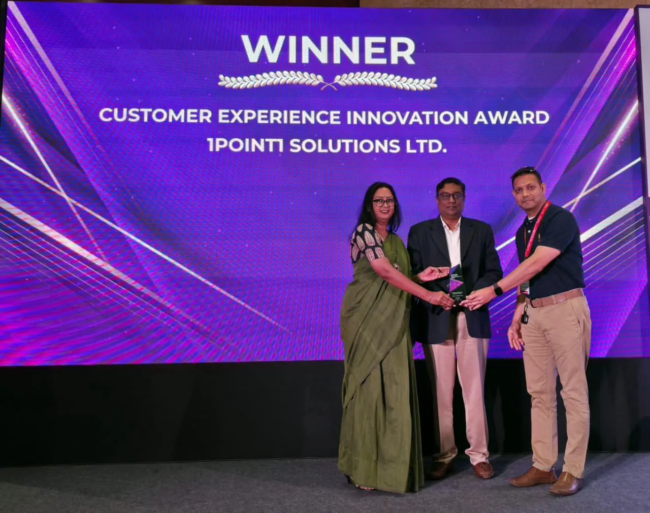 Three individuals receiving the Customer Experience Innovation Award on stage with a purple background screen.