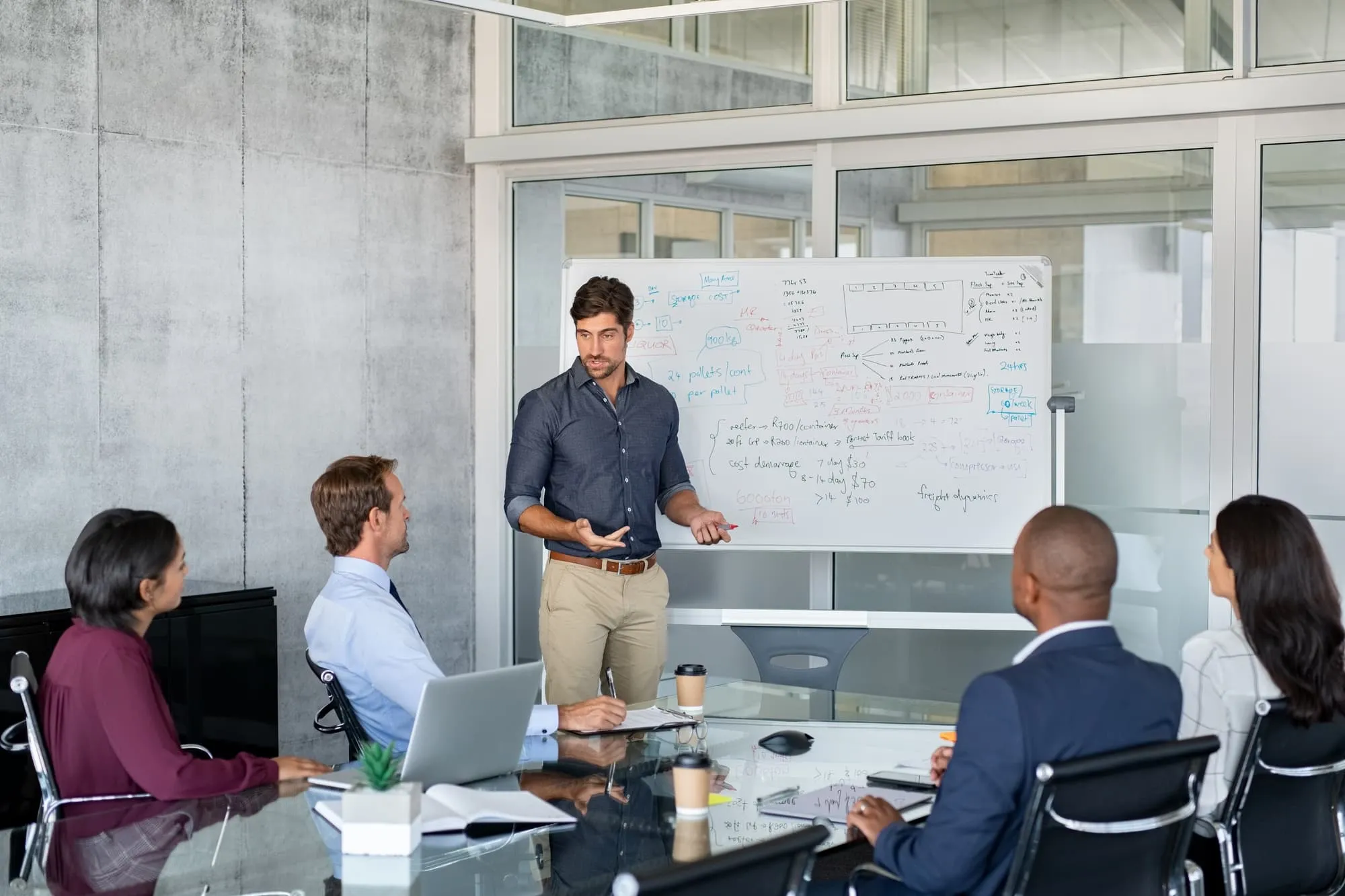 Company executive presenting new management strategy to team in conference room. Successful business man giving reports to his colleagues. Young manager presenting on white board his business plans.