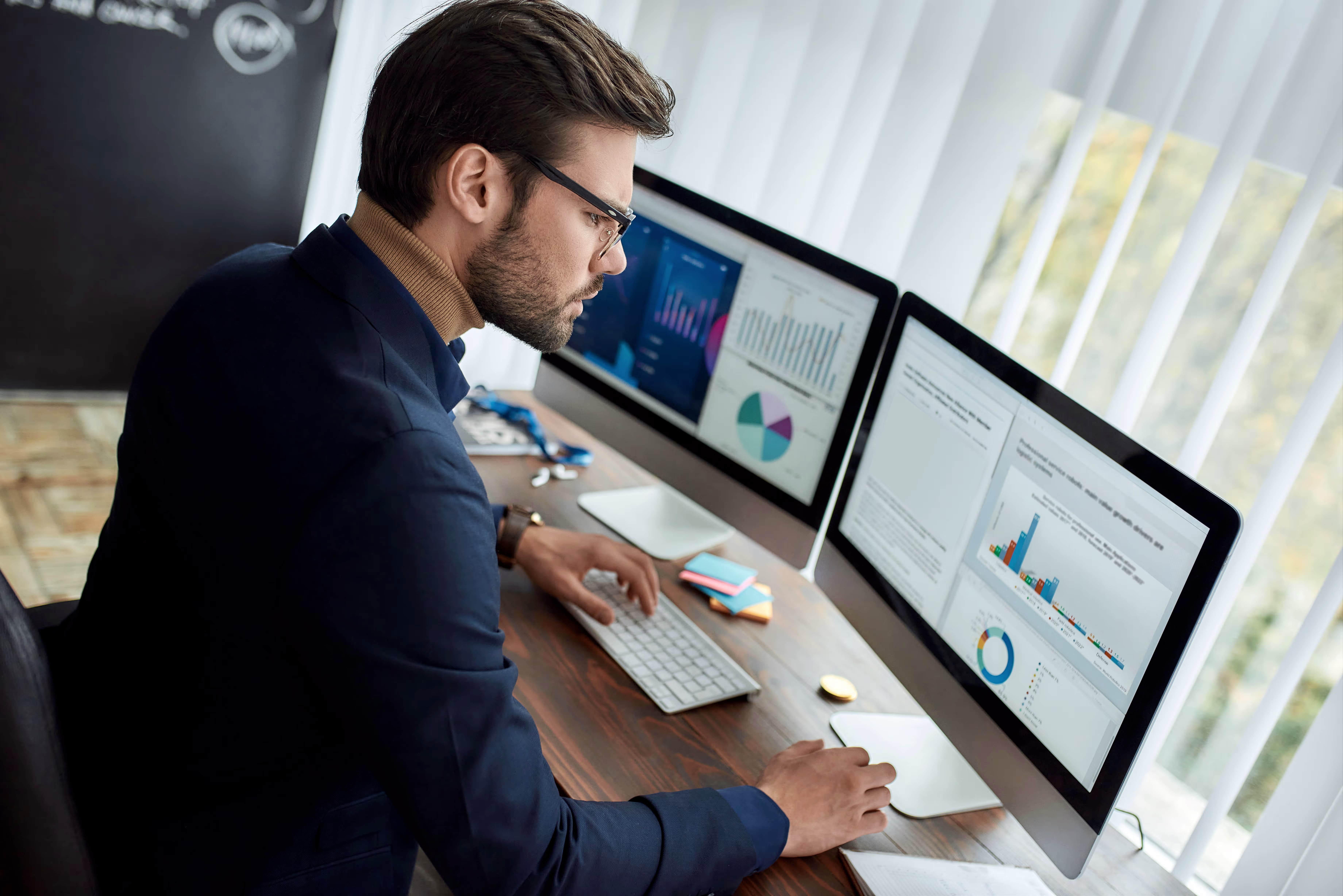 Man analyzing business data on dual monitors with charts and graphs.