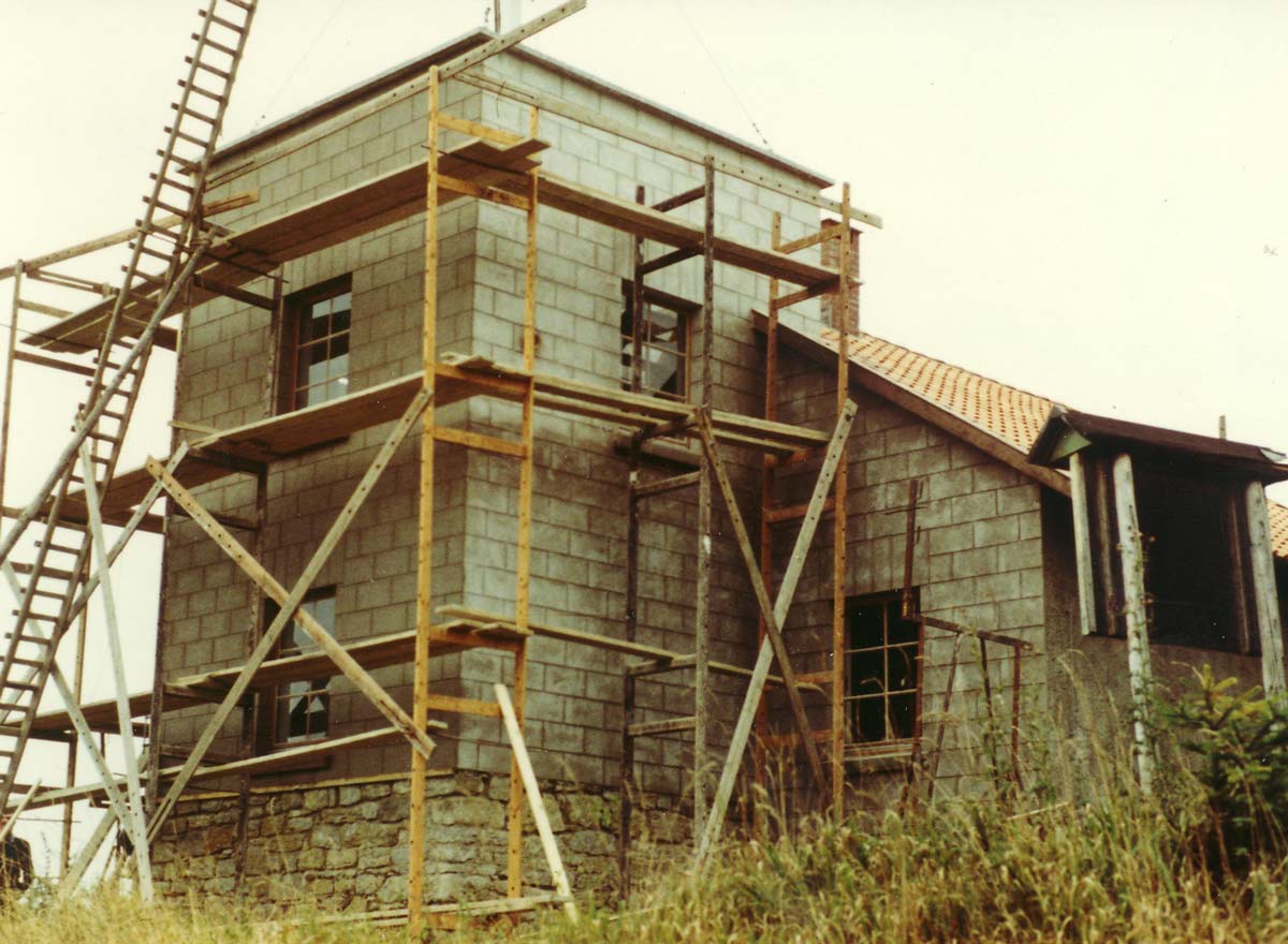 Der unter Bau stehender Turm der Telegrafenstation mit Sichtmauerwerk und Holzgerüst, umgeben von Gras.