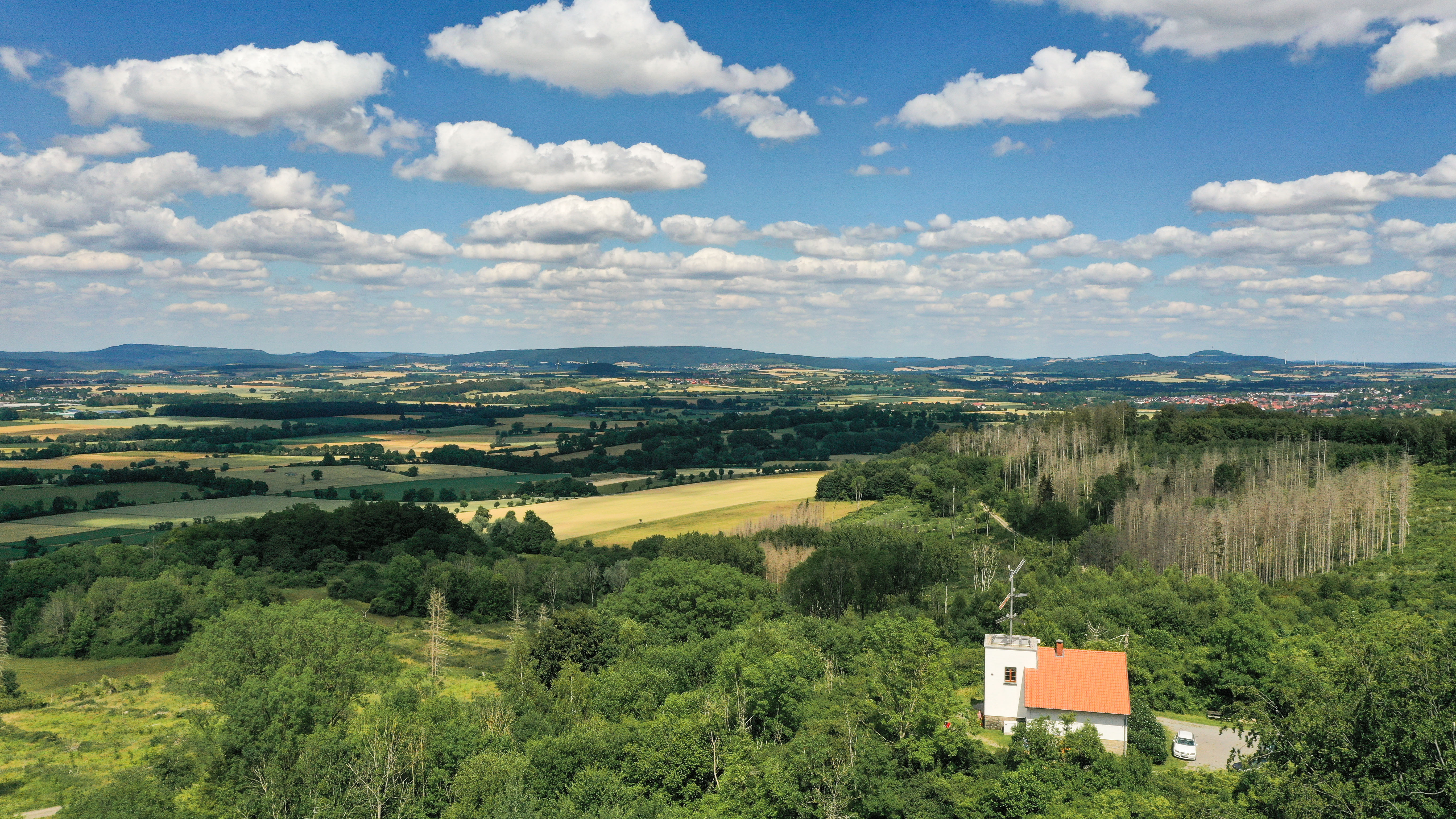 Landschaft mit Feldern, Wäldern und der Telegrafenstation 32 unter einem blau bewölkten Himmel.