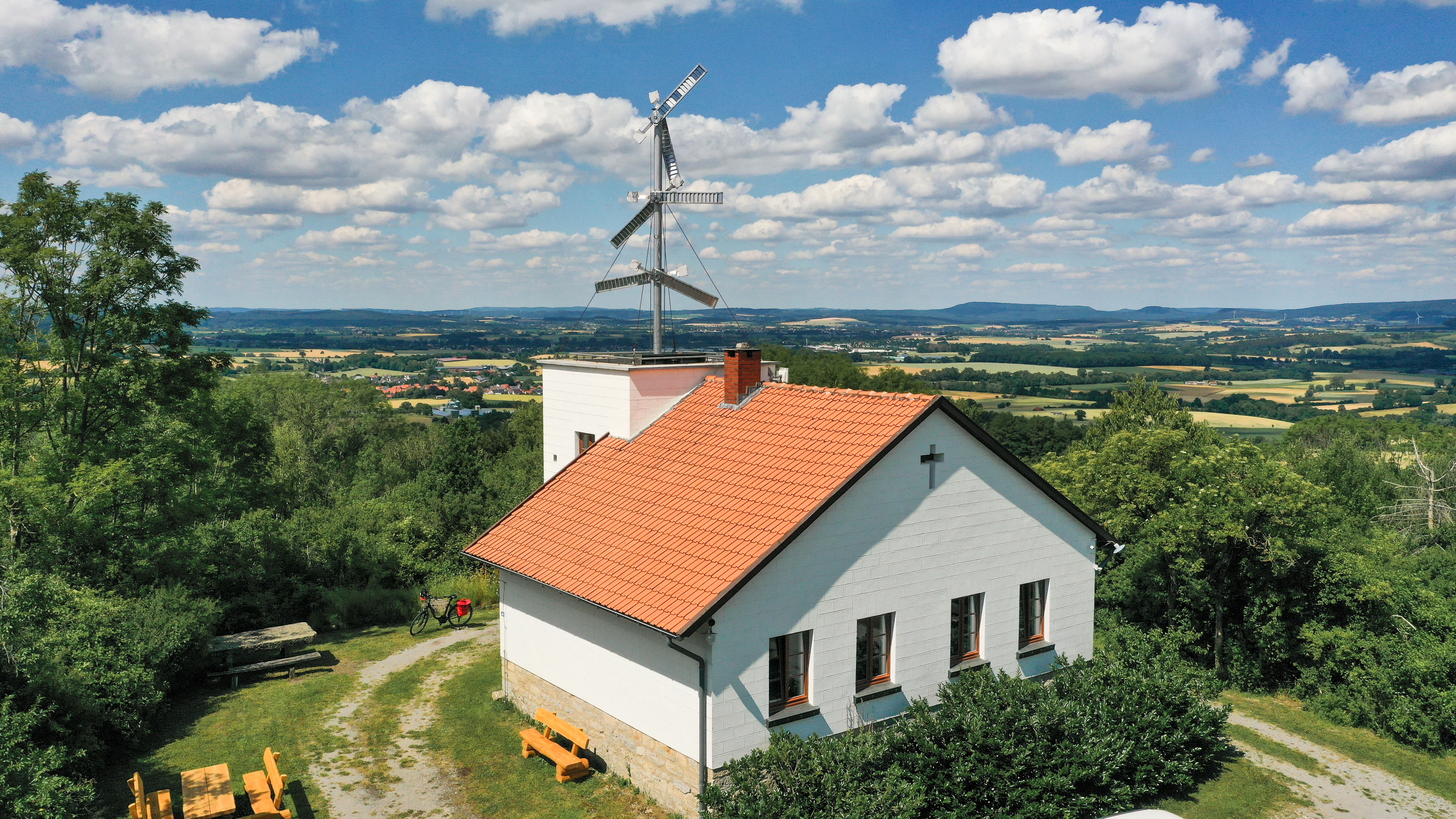 Telegrafenstation 32 auf einem Hügel mit Wald, Picknicktischen und weitem Blick über Felder unter blauem Himmel mit Wolken.