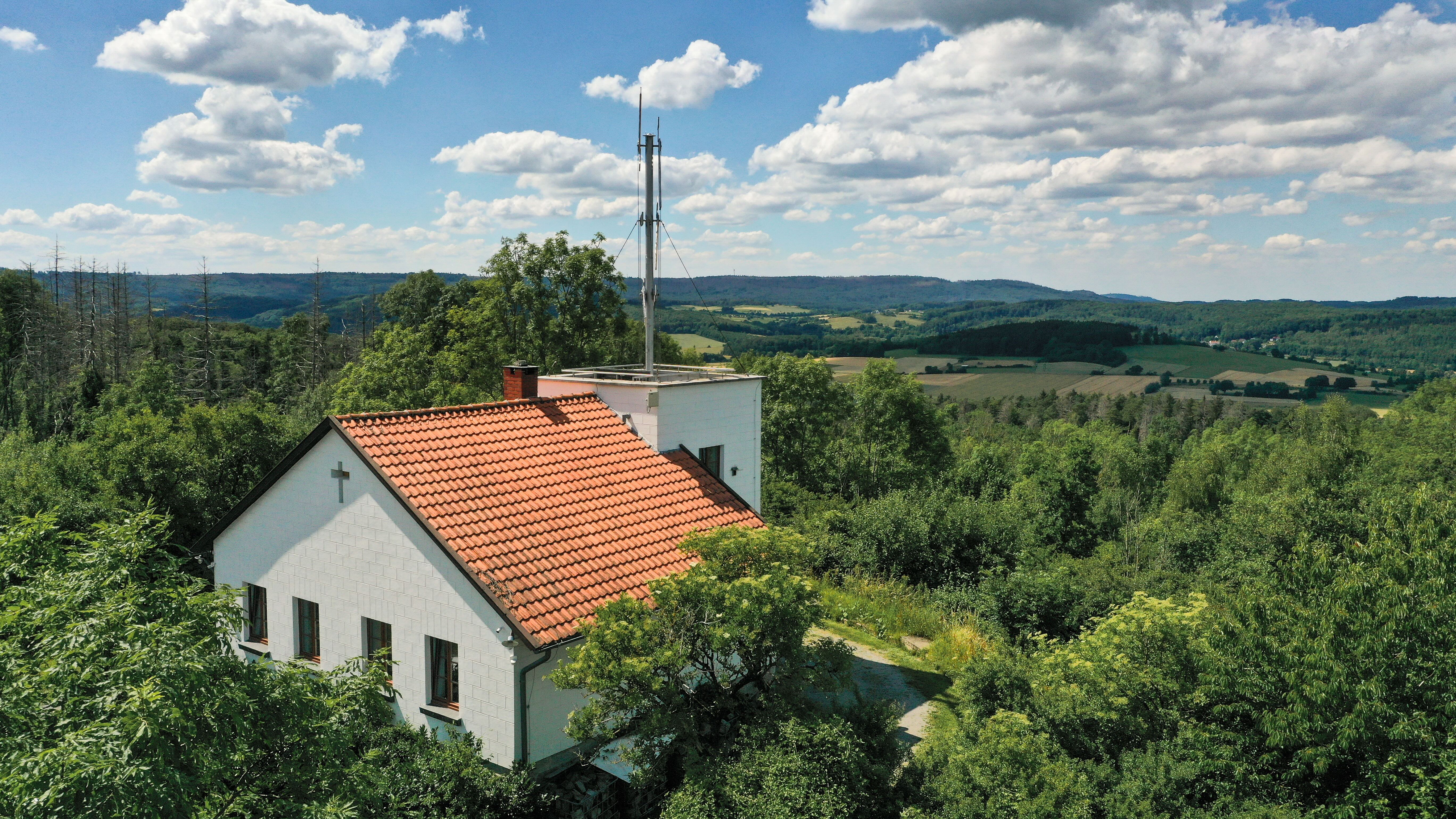 Telegrafenstation 32 umgeben von grünem Wald und dahinter hügelige Landschaft unter blauem Himmel mit Wolken.