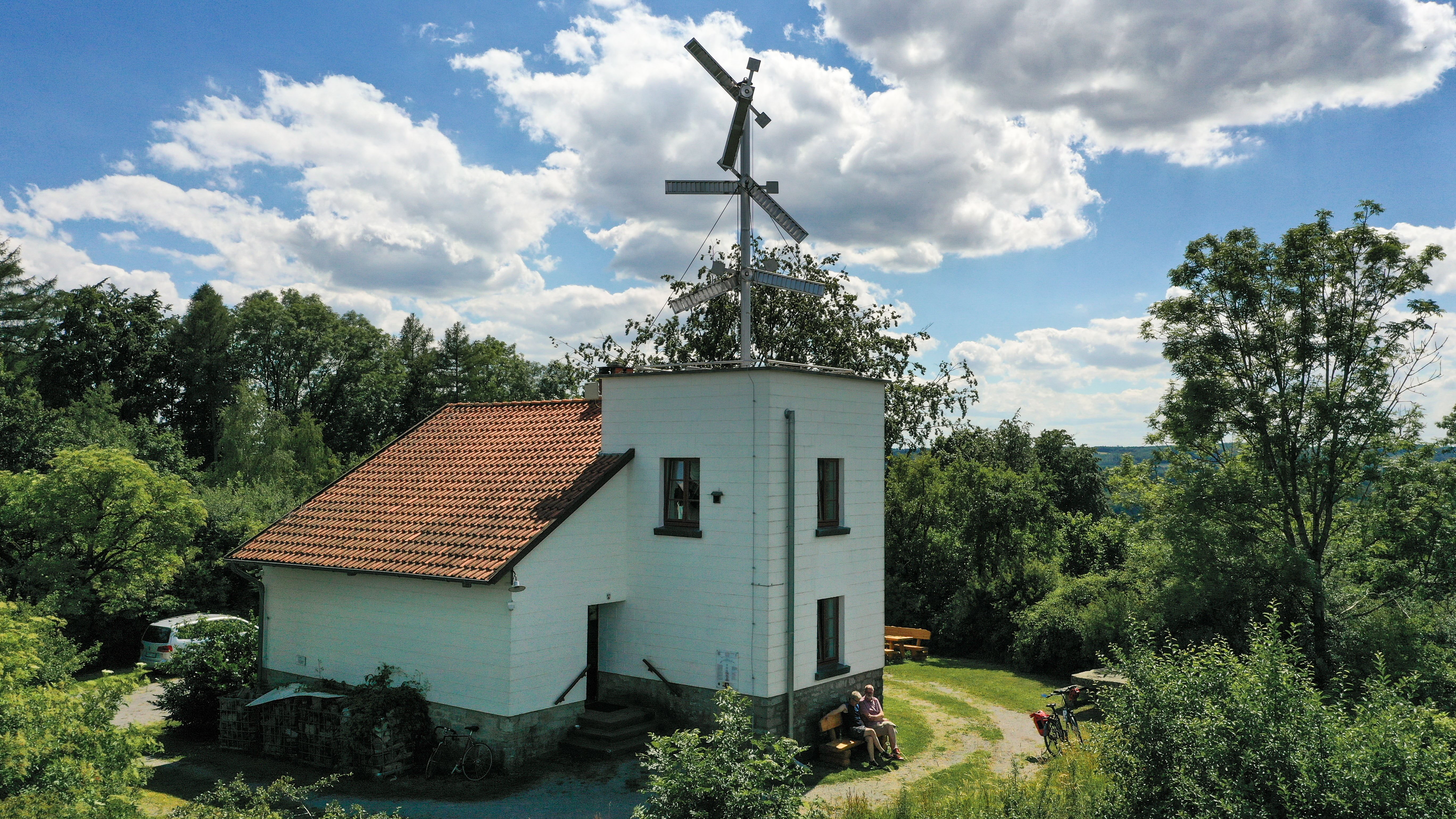 Telegrafenstation 32 umgeben von Bäumen, mit zwei Personen auf einer Bank im Schatten.