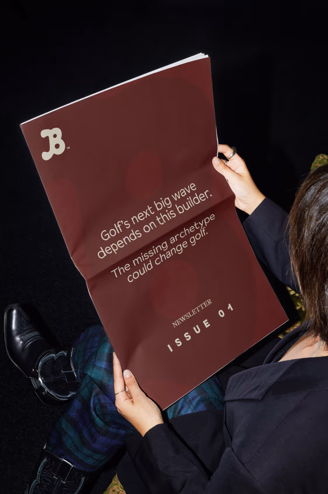 Person holding a maroon newsletter titled 'Golf's next big wave depends on this builder, Issue 01'.