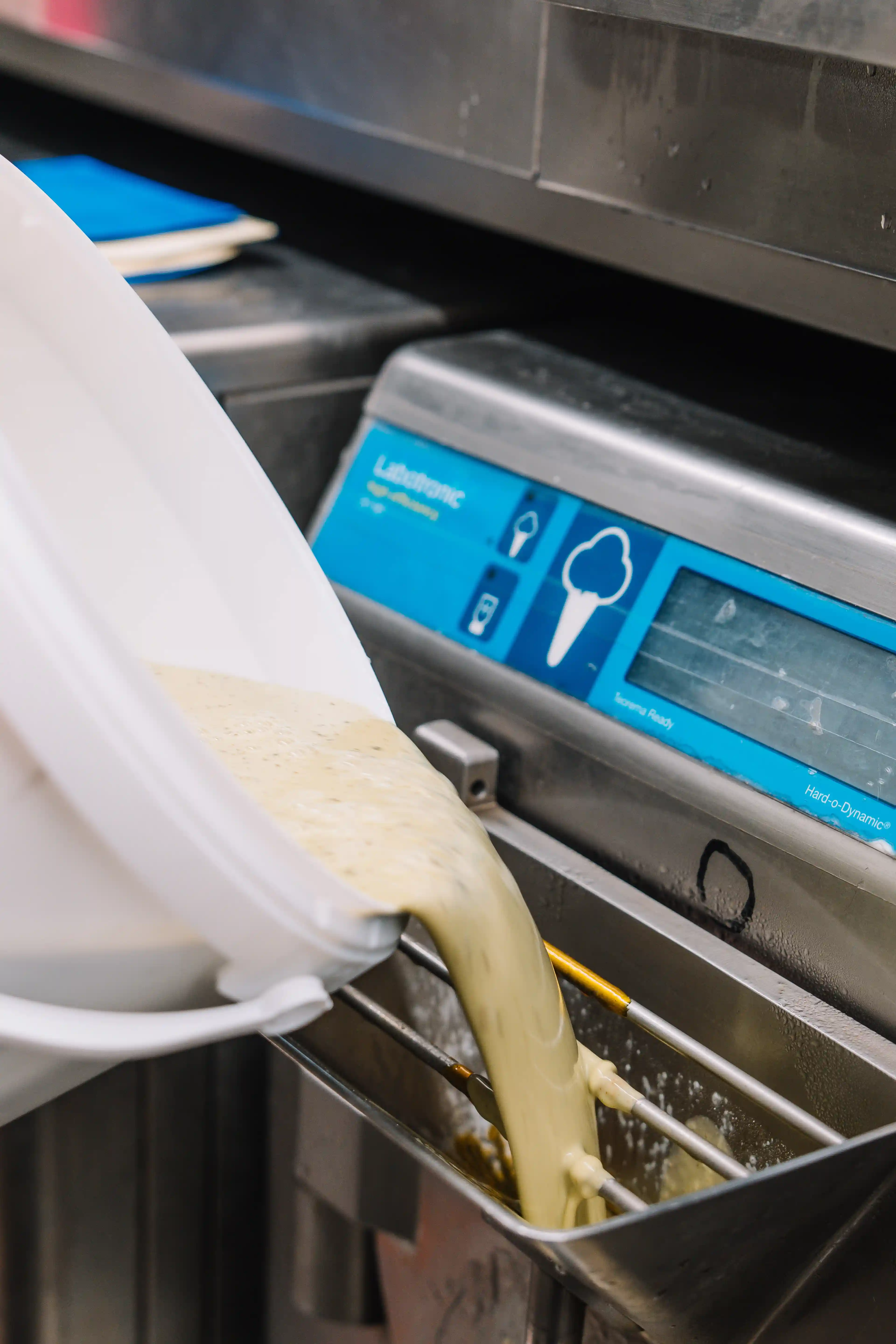 Pouring creamy ice cream mixture into a batch freezer machine for processing.