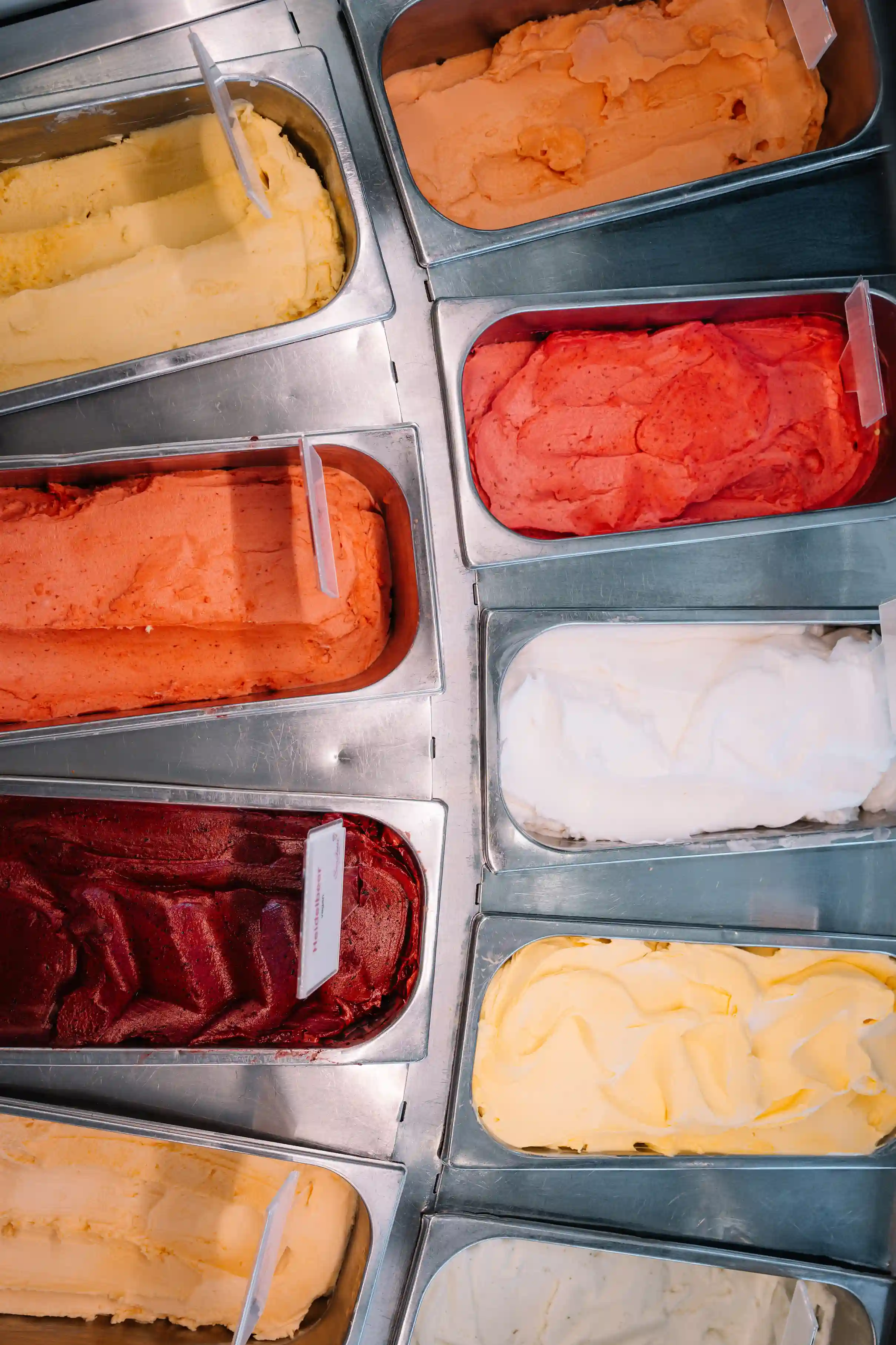 Reihen mit verschiedenfarbigem Eis (orange, rot, creme) in Metallbehältern der Eistheke