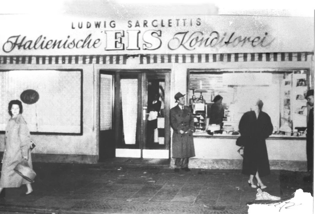 Historisches Schwarz-Weiß-Foto der Sarcletti-Ladenfront mit Schriftzug, Passanten davor