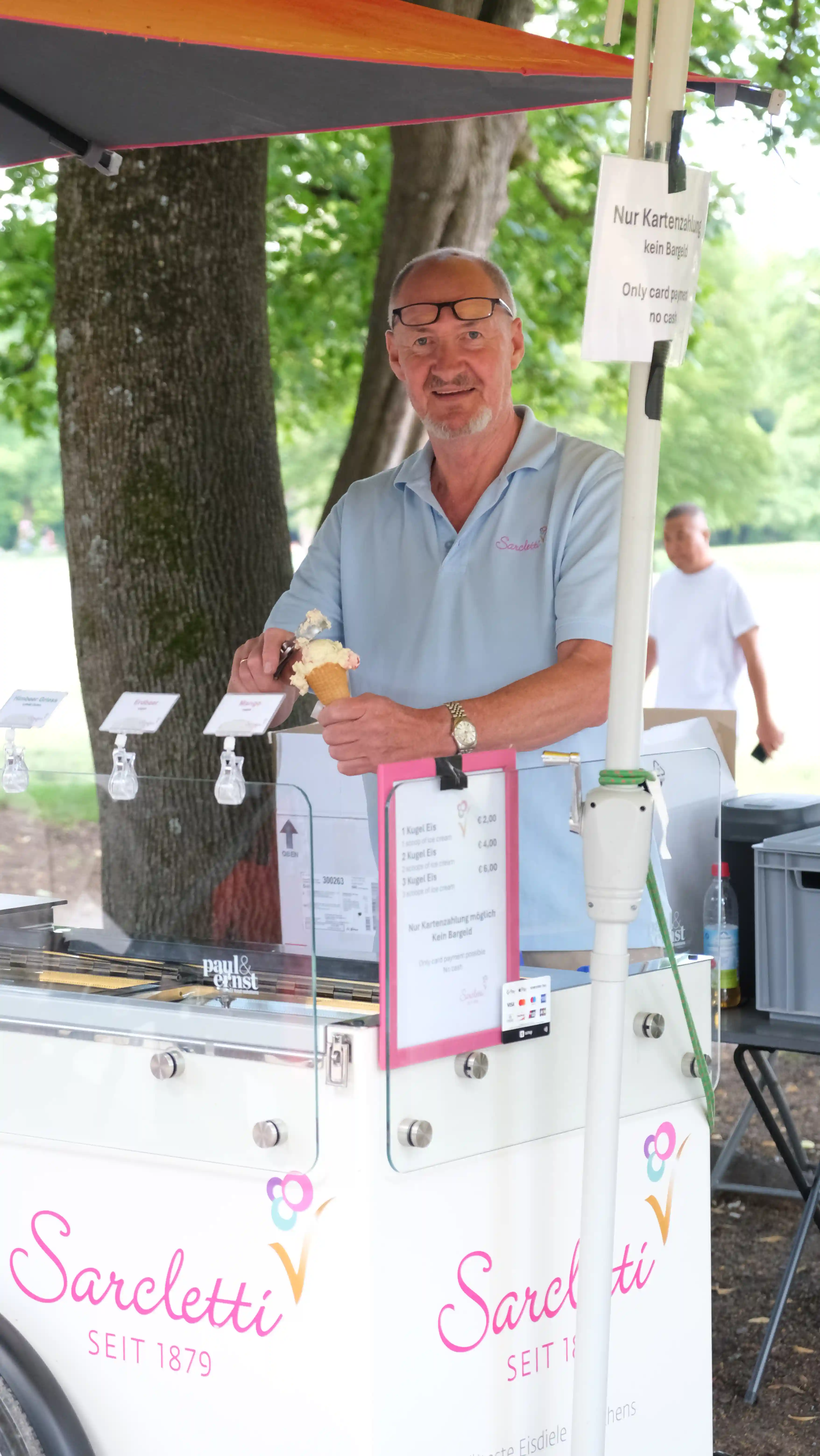 Sarcletti-Mitarbeiter am mobilen Eisstand mit Logo-Schürze im Englischen Garten München