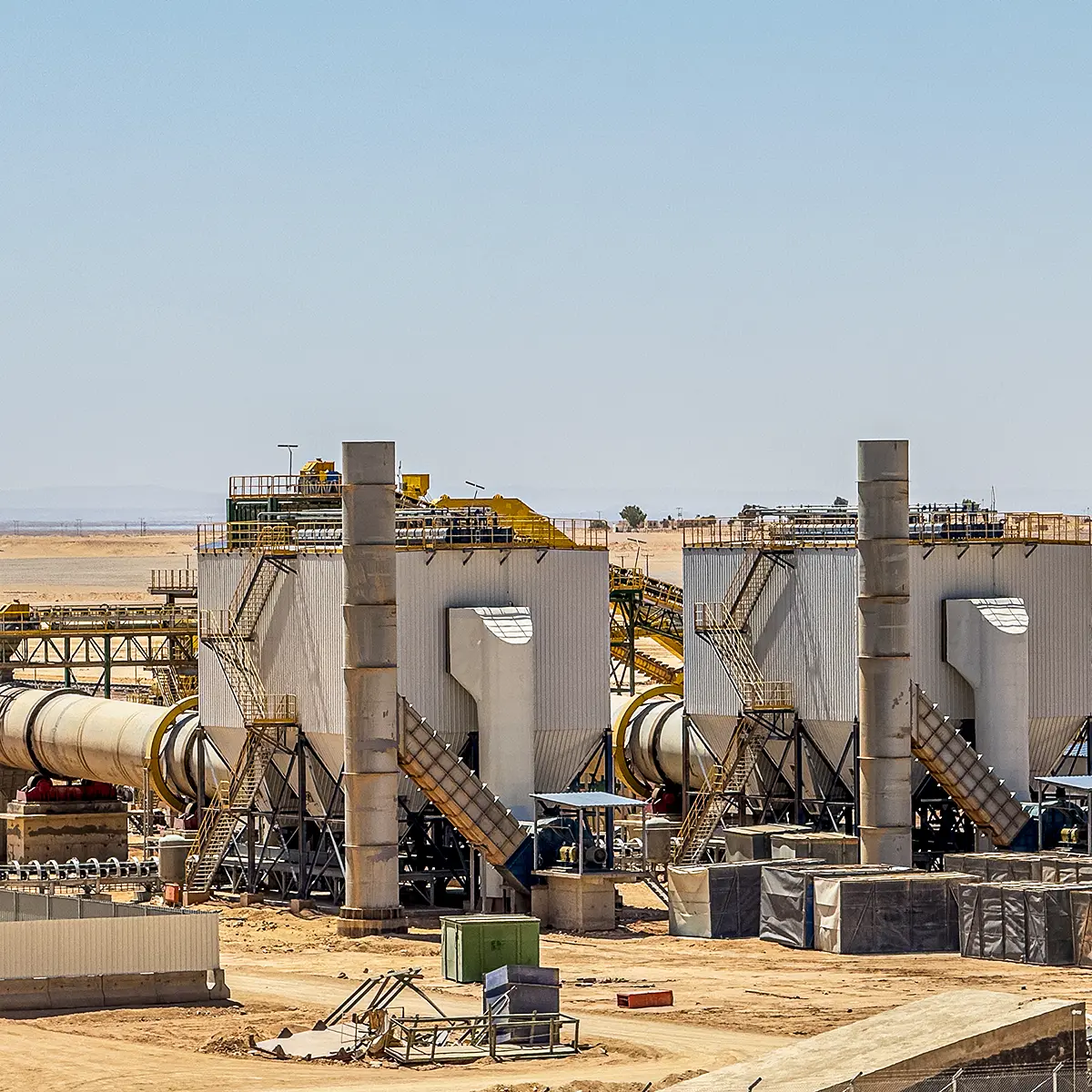 Industrial drying facility with large rotary kilns and tall exhaust stacks in a desert setting.