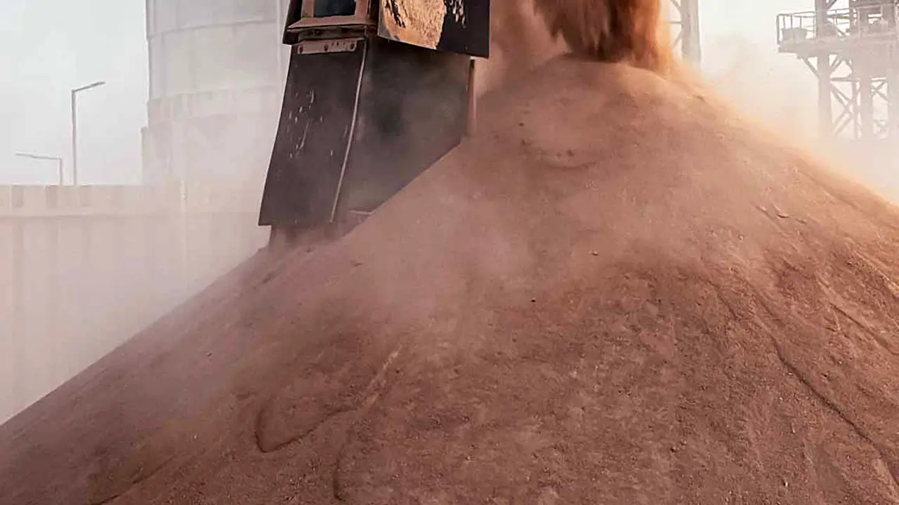 Industrial chute pouring a large mound of dry phosphate concentrate in an outdoor facility.