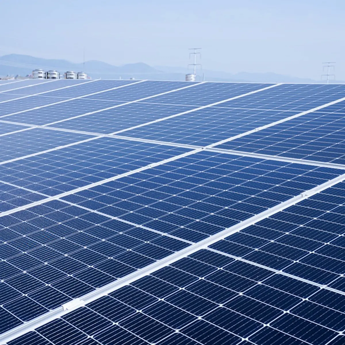 Large array of blue solar panels under a clear sky with distant mountains in the background.