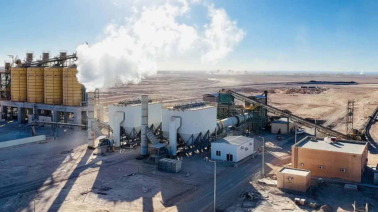 IDMI phosphate beneficiation plant in southern Jordan with large silos and equipment emitting white steam under a clear blue sky.