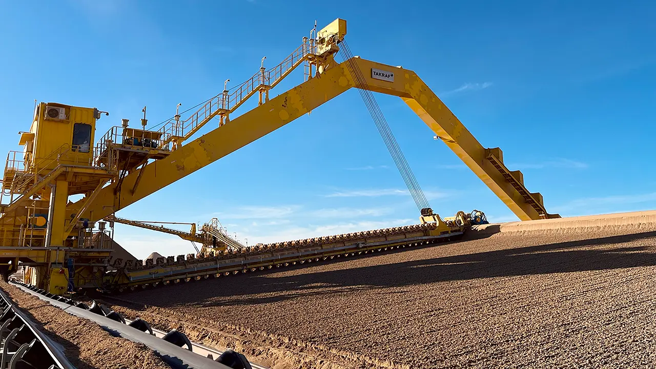 Large yellow industrial reclaimer machine under a clear blue sky.