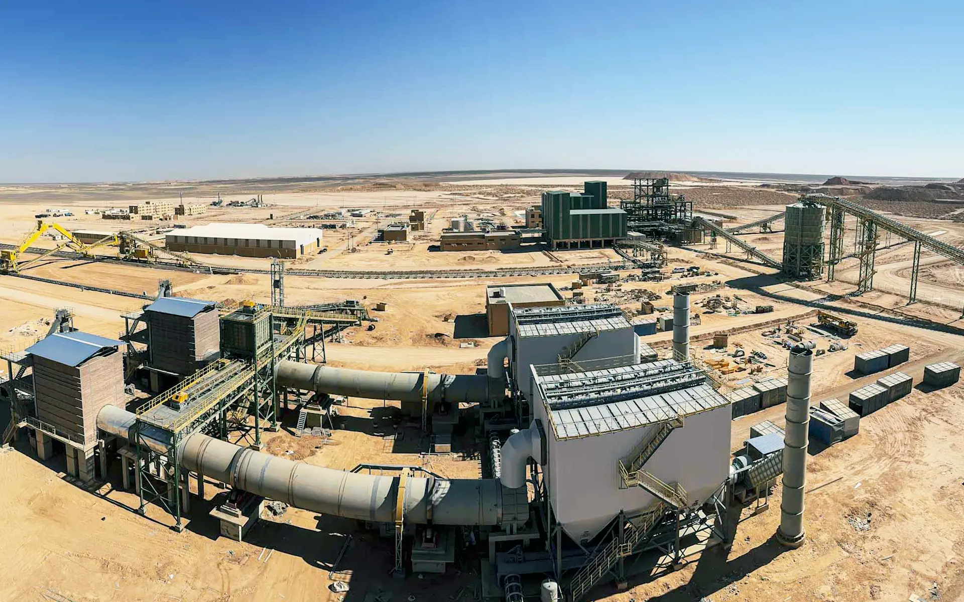 A large industrial rotary dryer system in a desert landscape with multiple interconnected cylindrical metal tubes and surrounding industrial buildings.