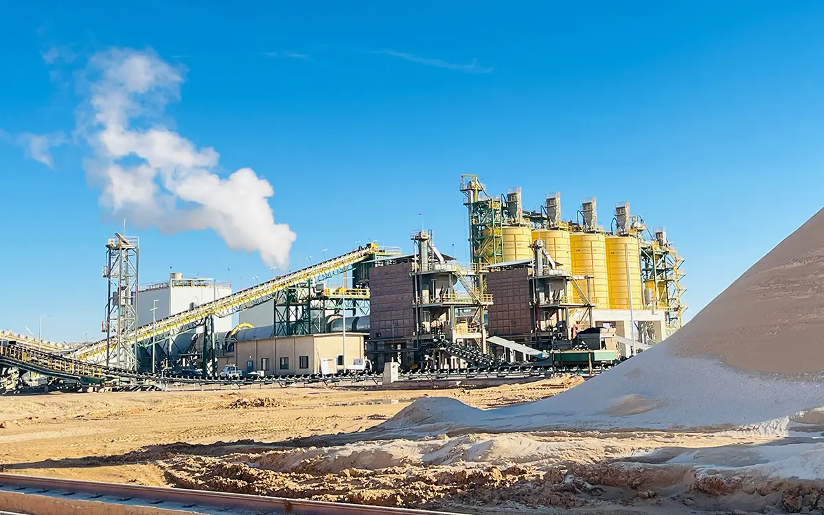 Dry phosphate concentrate storage silos and conveyor belts under a clear blue sky.