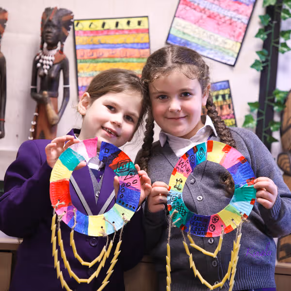 Two young girls holding colorful handmade paper crafts decorated with drawings and hanging strings.
