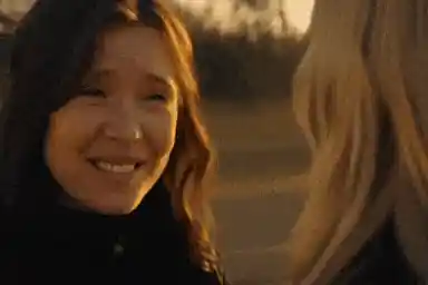A woman with long brown hair and light skin smiles at another woman