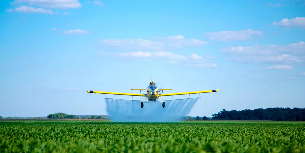 Air Tractor AT-502B aircraft spraying chemicals over a green field under a blue sky.