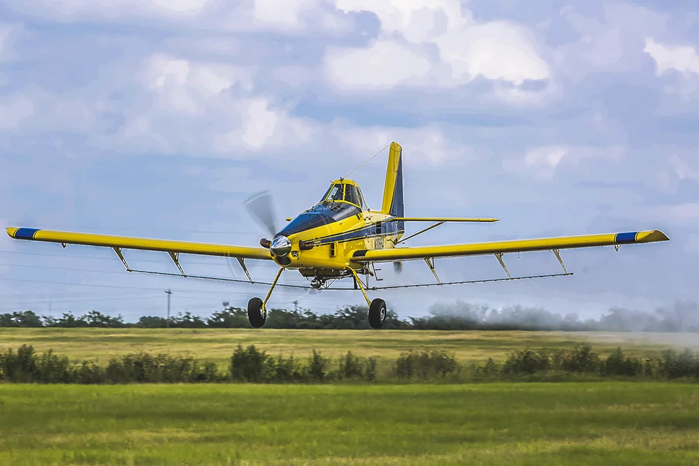 Yellow Air Tractor 502XP agricultural aircraft sitting on green farmland under cloudy sky.