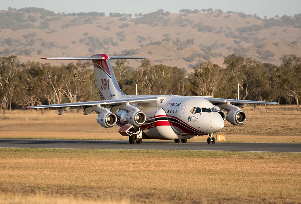 White and red Conair C-GVFK aorcraft taxiing on runway with grassy fields and hills in background.