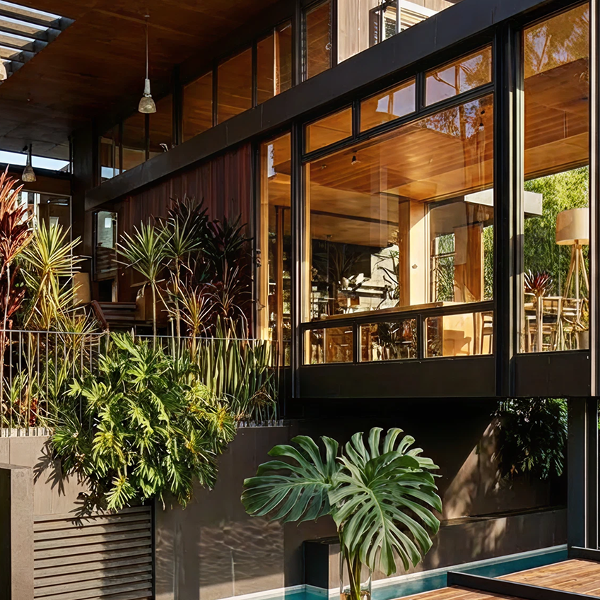Modern kitchen with a large marble island, a glass vase holding large green leaves, and an open sliding door leading to an outdoor garden area with plants.