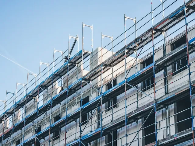 Construction scaffolding surrounding a multi-story building under construction against a clear blue sky.