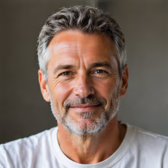 Smiling middle-aged man with salt-and-pepper hair and beard wearing a white shirt against a neutral background.