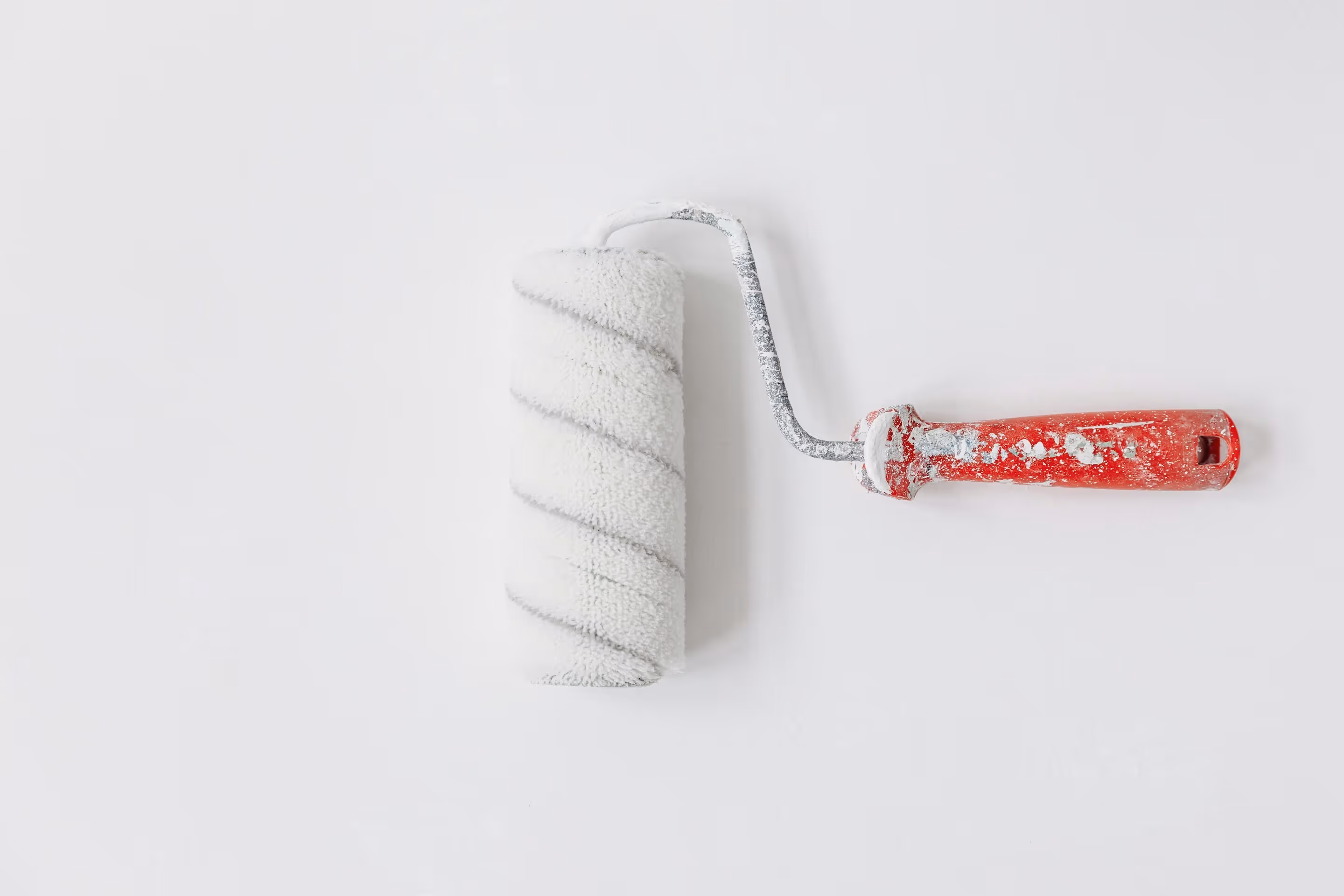 White paint roller with a red handle covered in dried paint on a white surface.