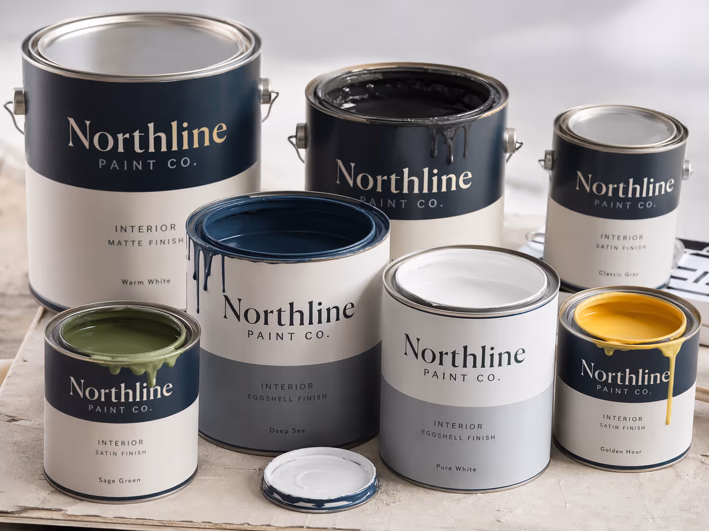 Seven cans of Northline Paint Co. interior paint in various finishes and colors, some open with paint dripping, on a white surface.