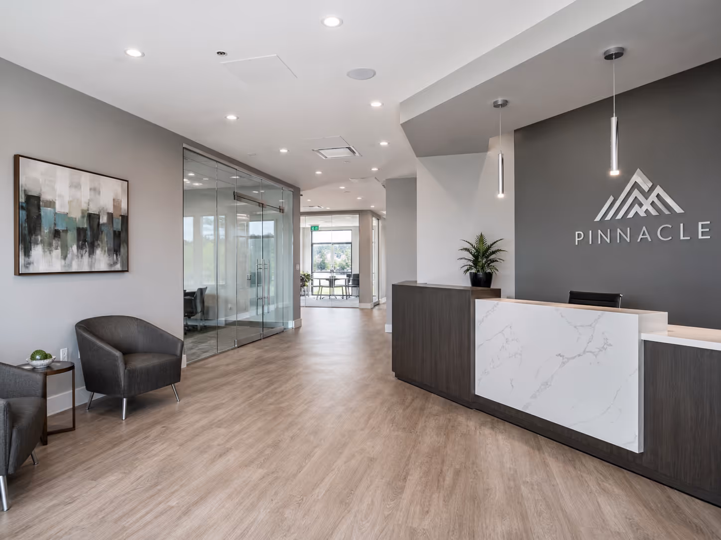 Modern office lobby with wooden flooring, a reception desk with Pinnacle logo, seating area with gray chairs, and glass-walled conference rooms.