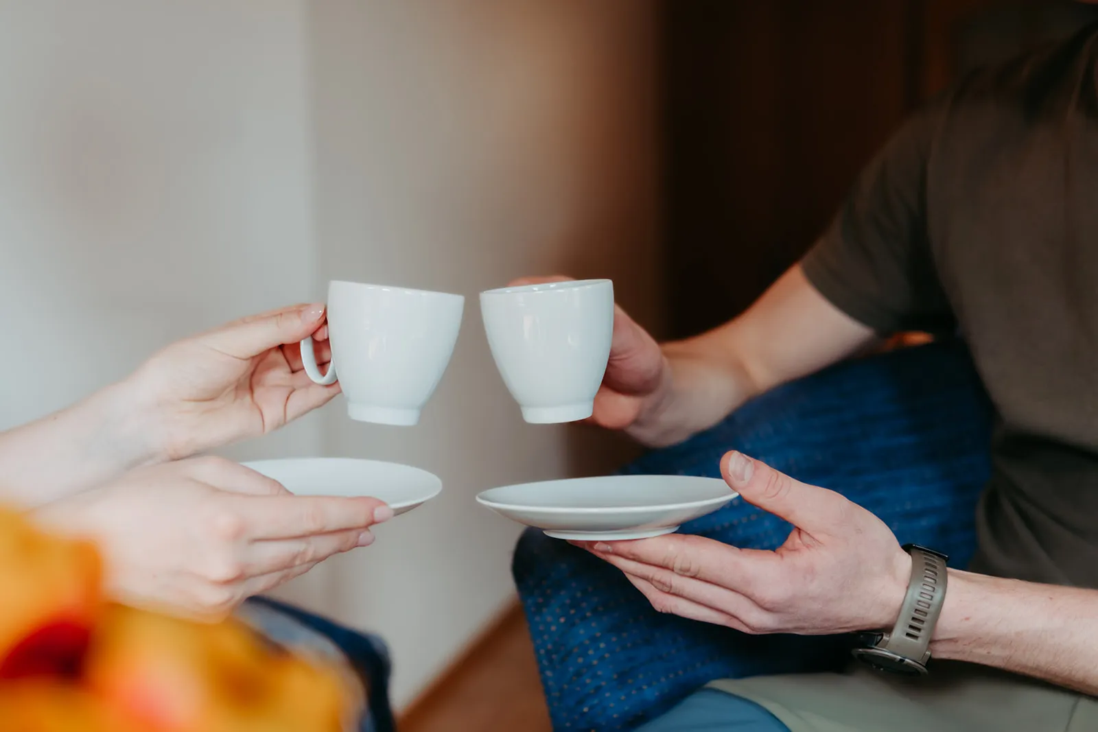 Zwei Personen stoßen mit weißen Tassen und Untertellern an.