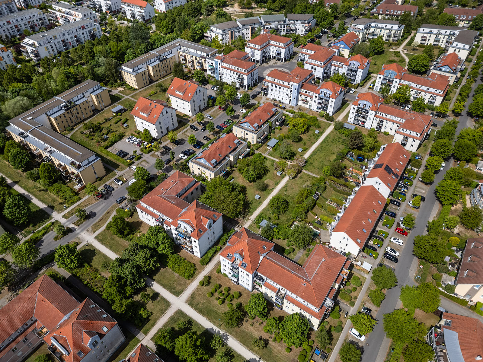 Luftaufnahme einer weitläufigen Wohnanlage mit begrünten Innenhöfen, Wegen und roten Ziegeldächern