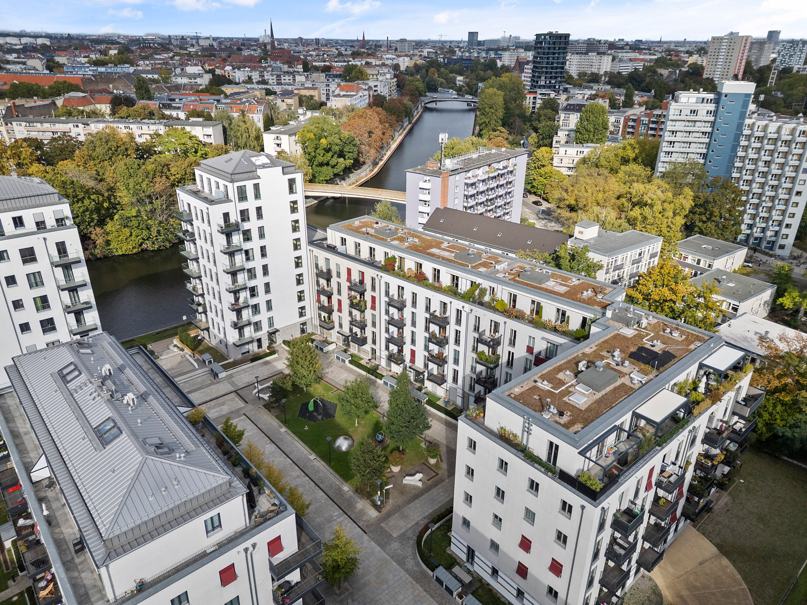 Luftaufnahme einer modernen Wohnanlage in Berlin mit begrüntem Innenhof, Dachterrassen und angrenzendem Wasserlauf
