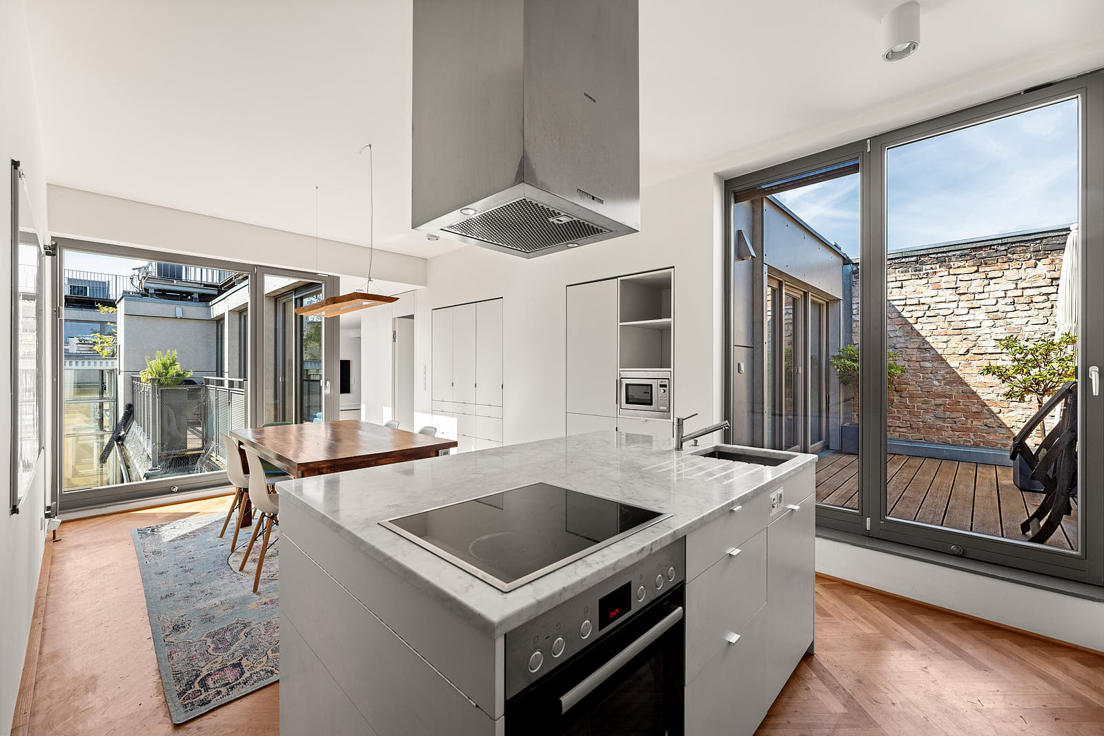 Helle moderne Küche mit Kochinsel, Essbereich, großen Fensterflächen und Zugang zur Dachterrasse