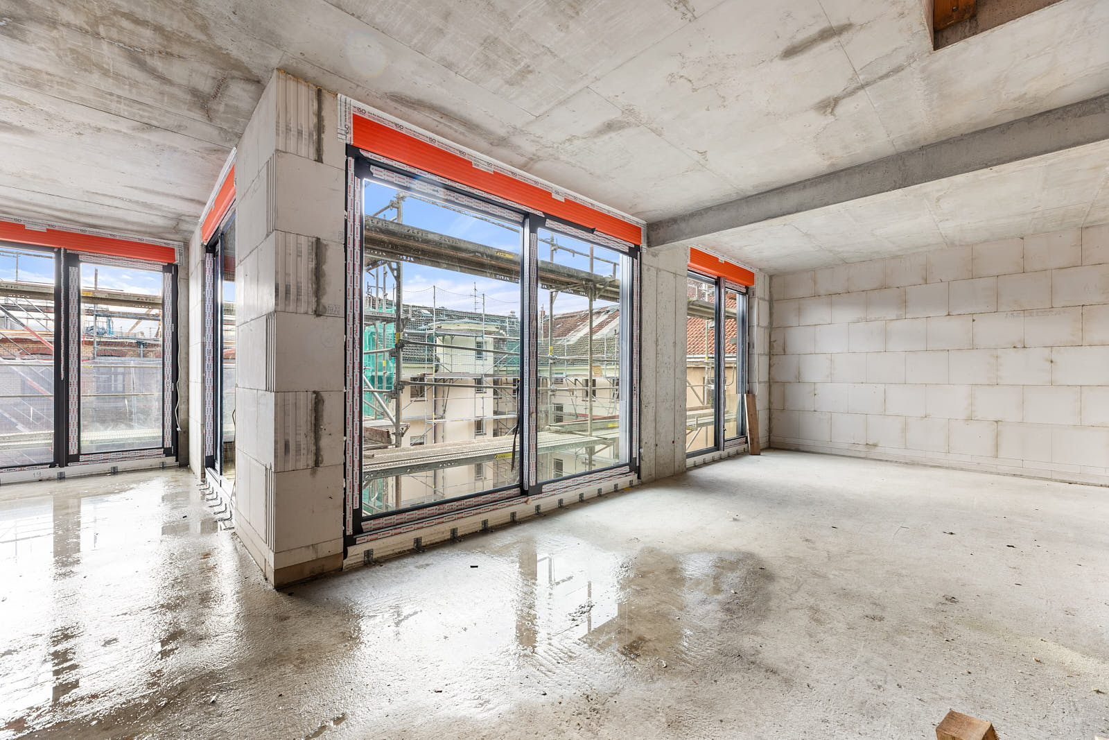 Innenraum eines Wohngebäudes im Rohbau mit großen Fensterflächen und Blick auf die Baustelle