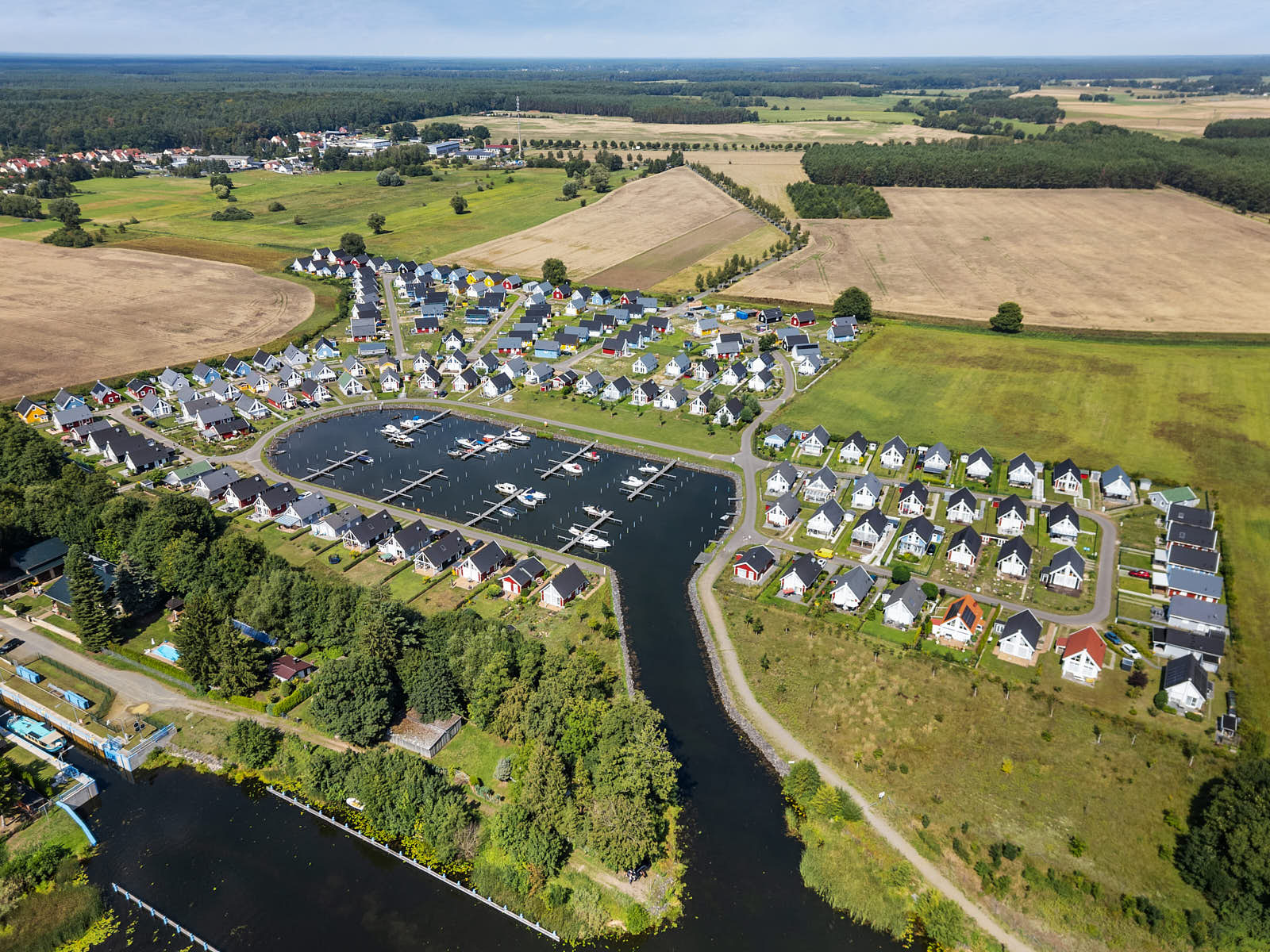 Luftaufnahme einer Wohnanlage mit Yachthafen, Einfamilienhäusern und umliegender Landschaft