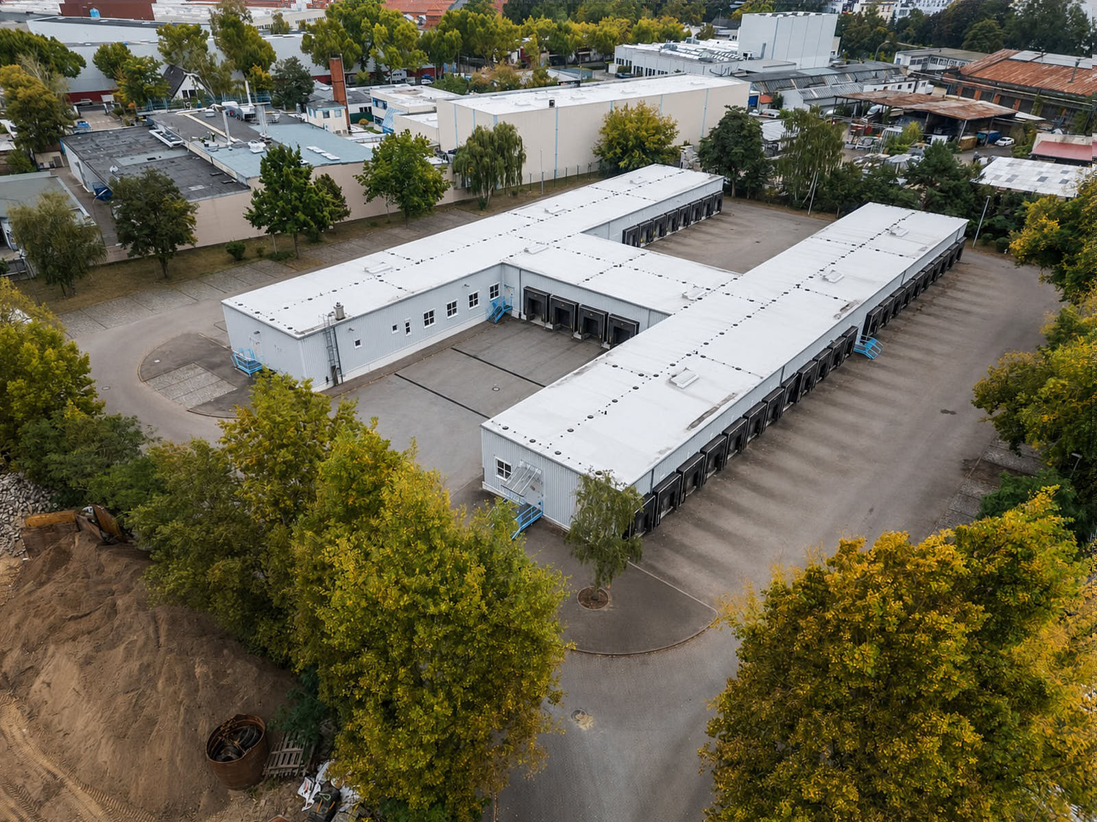 Luftaufnahme eines Gewerbe- und Logistikgebäudes mit Ladezonen, Hofflächen und umgebender Industrieanlage