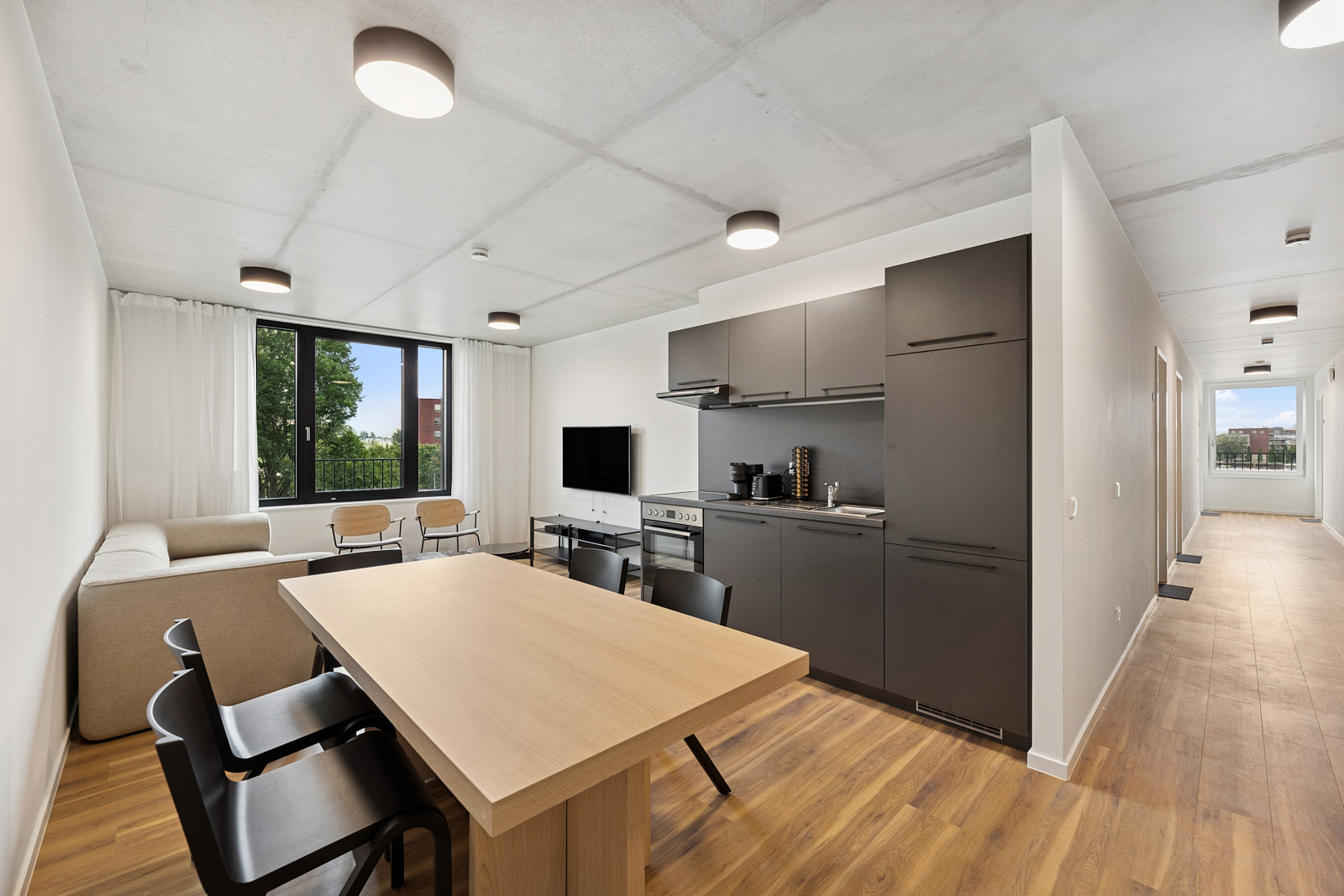 Moderner Wohn- und Essbereich mit integrierter Küche, großem Esstisch und Sichtbetondecke