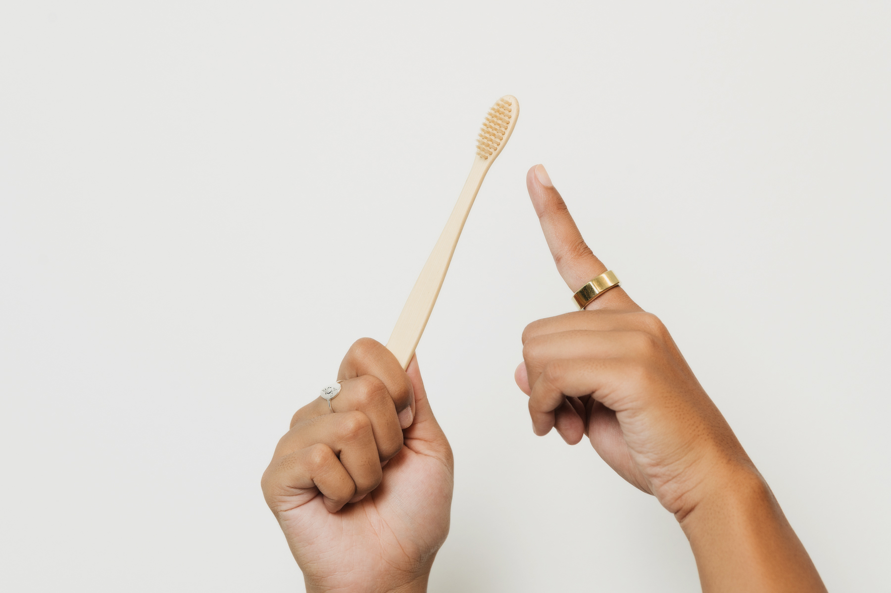 Person holding a bamboo toothbrush in one hand while pointing at it with the index finger of the other hand.