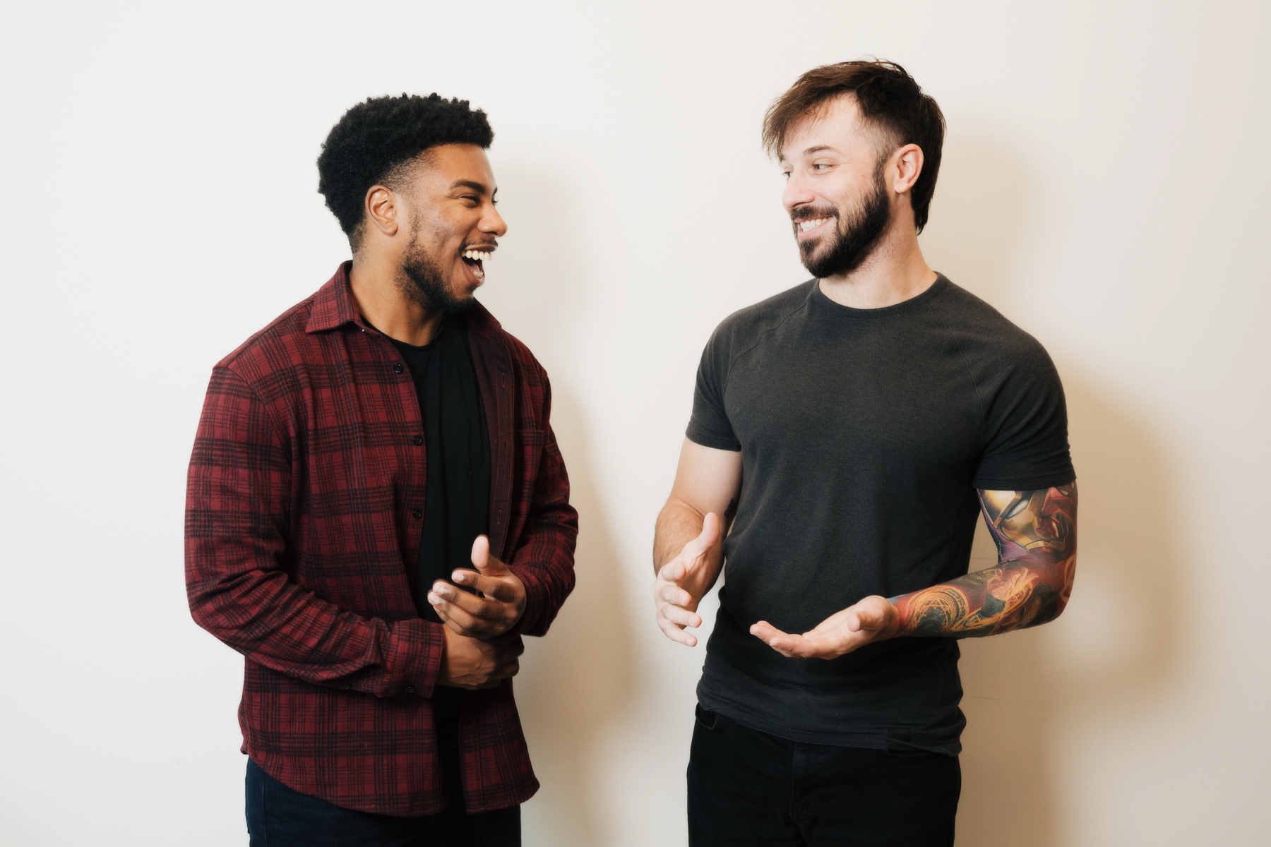 Two men smiling and having a lively conversation against a plain light background.