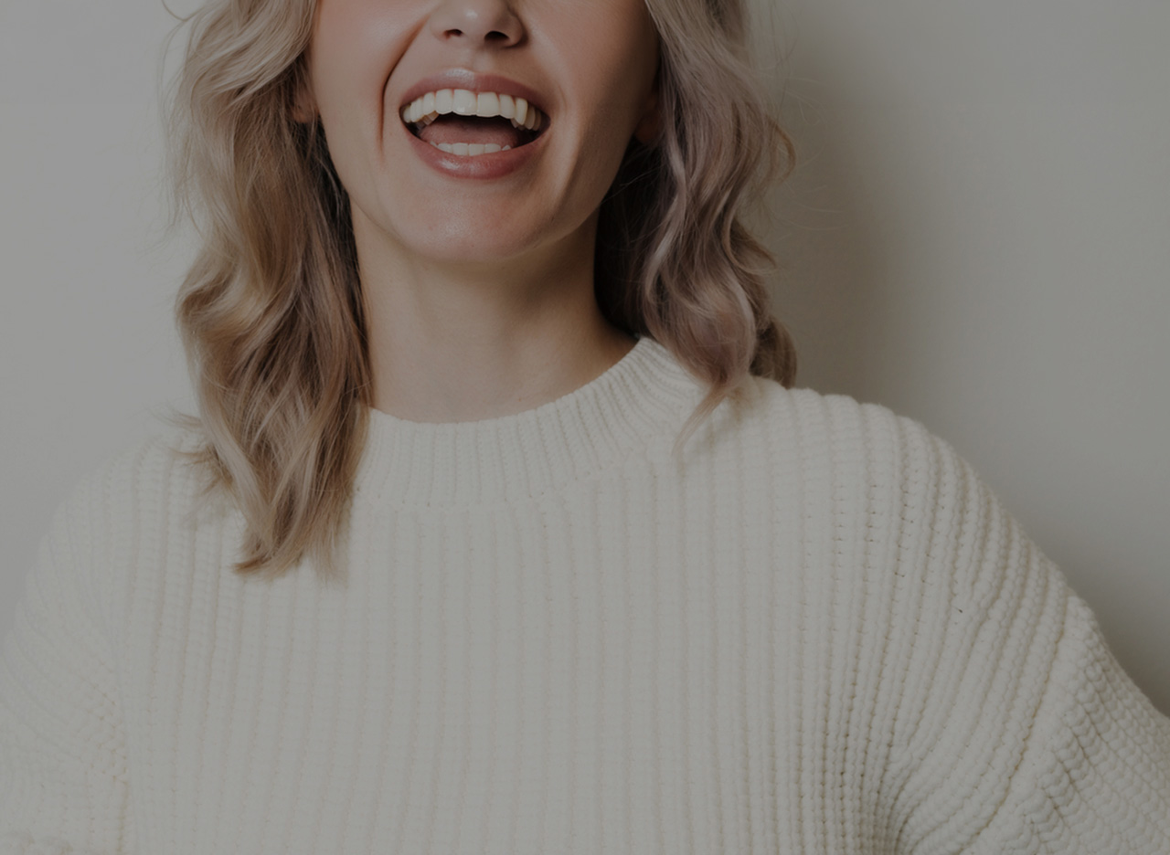 Close-up of a woman smiling with her mouth open, wearing a white knitted sweater.